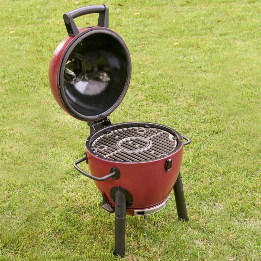 a red kamado grill with the lid raised in a grassy backyard