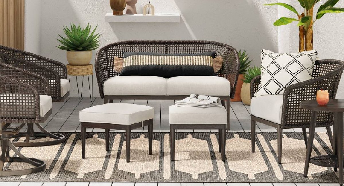 5 piece wicker set displayed in backyard with rug on the ground and plants surrounding