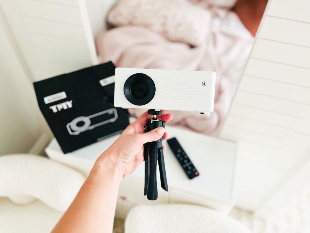 TMY Mini Projector with Tripod in woman's hand with box behind it in living room