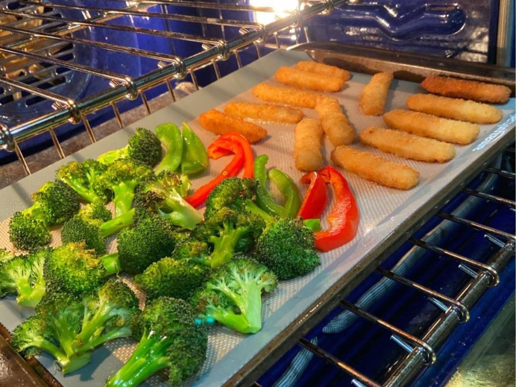 A sheet pan of broccoli, bell peppers and fish sticks in the oven