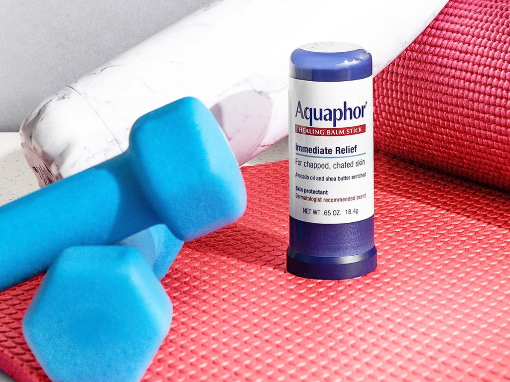 Aquaphor Healing Balm Stick on yoga mat next to hand weights