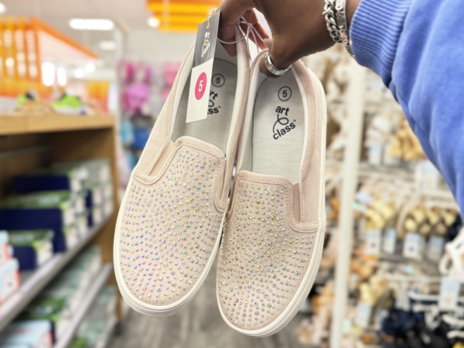 holding up a pair of light pink rhinestone slip-on sneakers