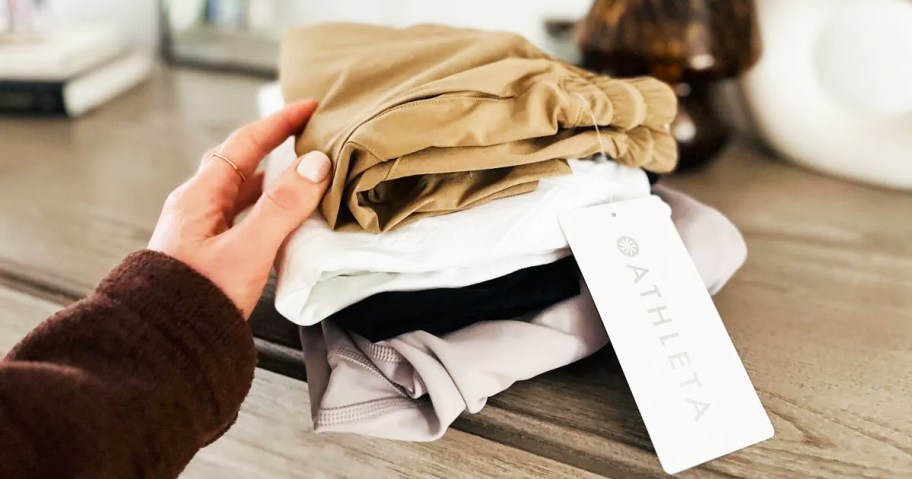 woman's hand touch a stack of folded athleta clothing