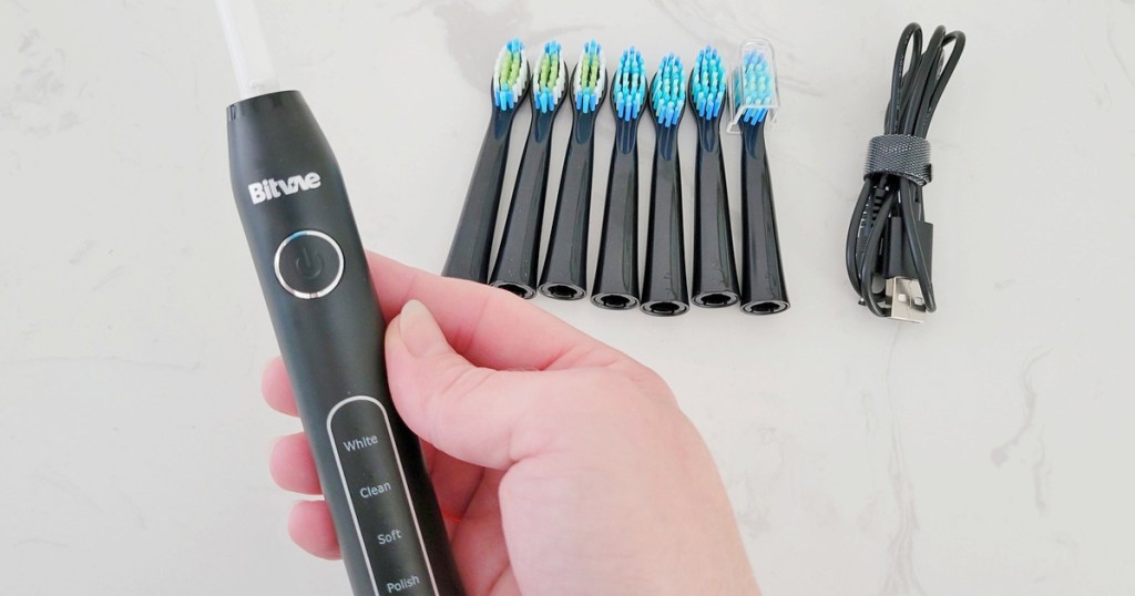 hand holding a Bitvae toothbrush with replacement heads and recharging cord in the background