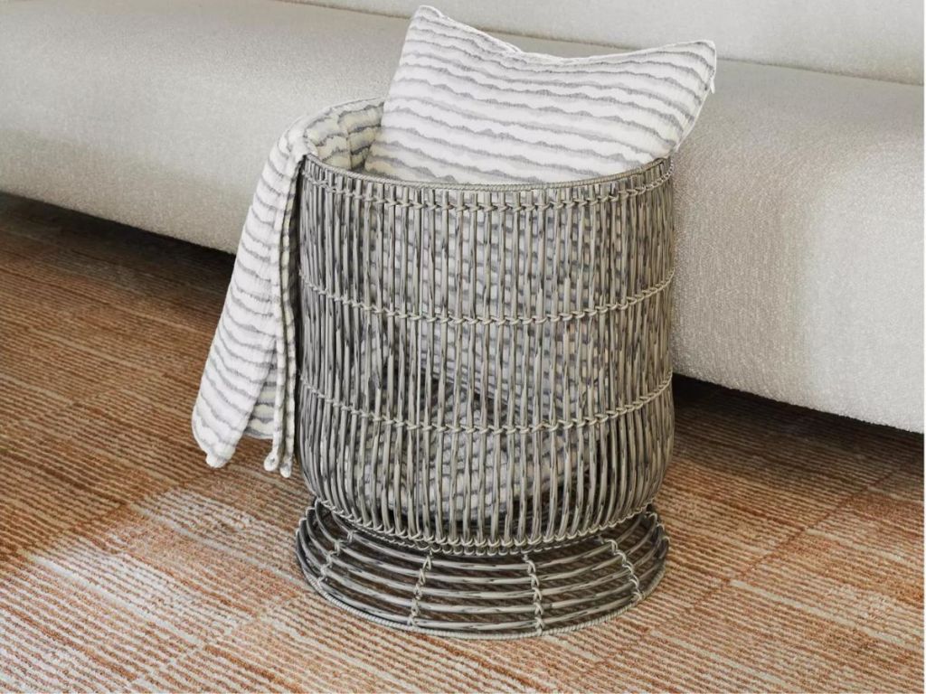 A gray rattan storage table with a pillow and blanket in it 