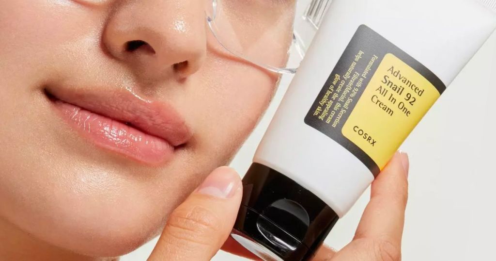 a woman holding a tube of COSRX Advanced Snail 92 All In One Cream next to her cheek