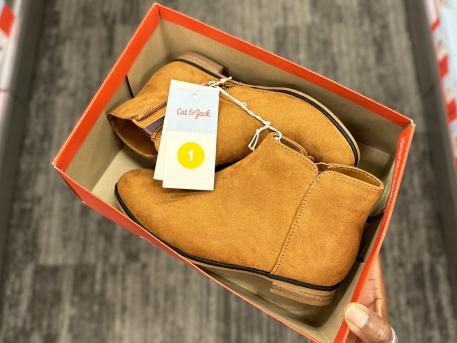hand holding a shoe box with brown booties inside