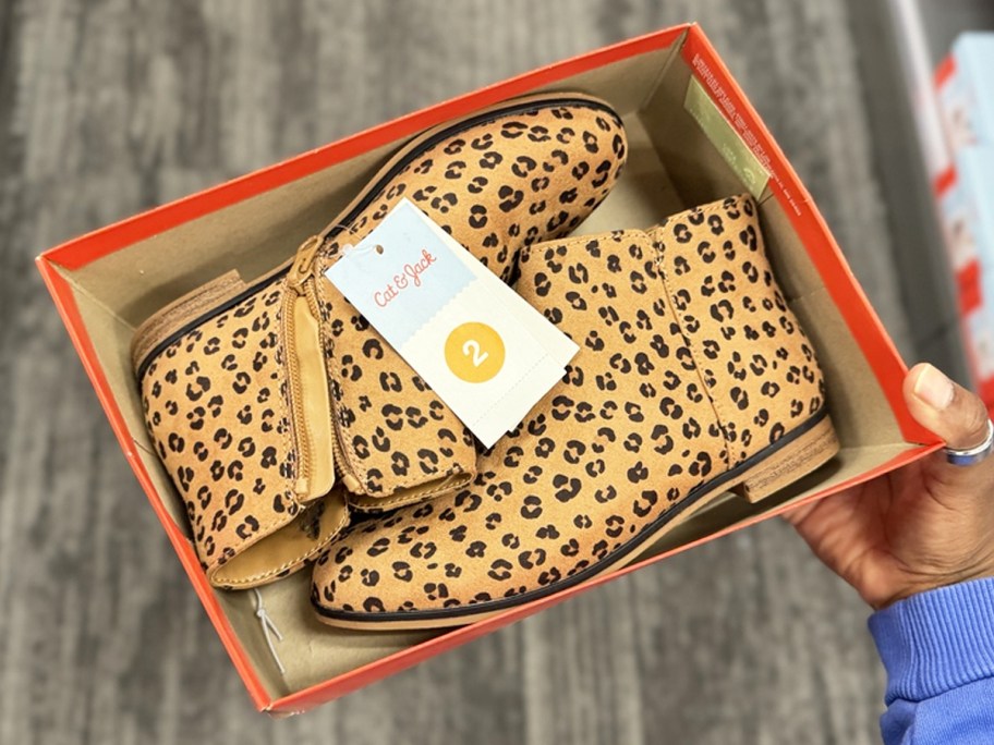 hand holding a shoe box with leopard print booties inside