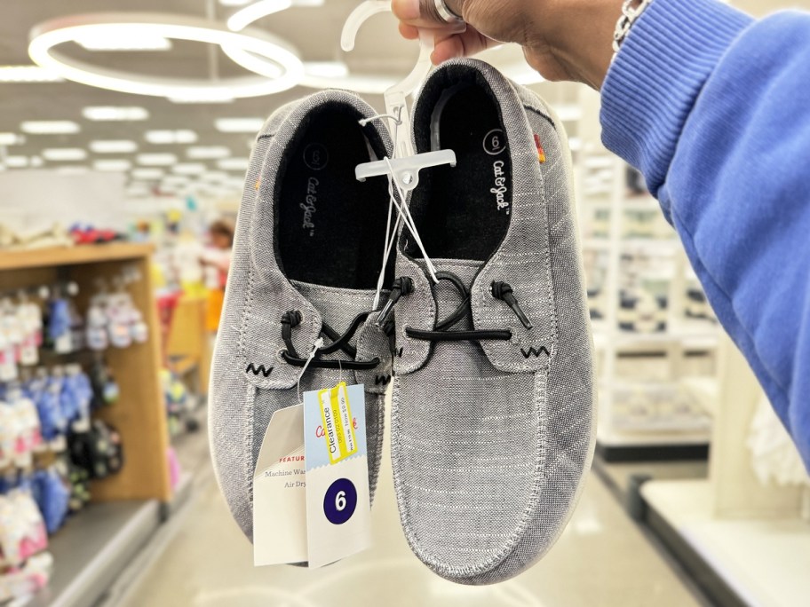holding up a pair of grey slip-on kids shoes in store