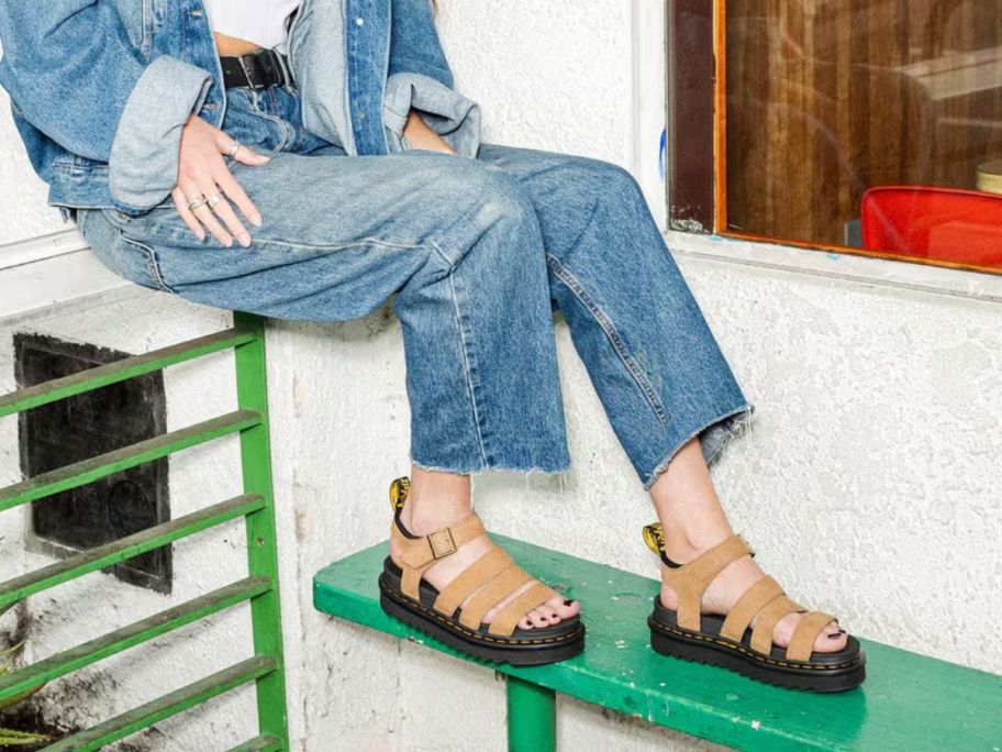 Woman sitting on a railing wearing Dr. Martens Blaire Nubuck Leather Sandals