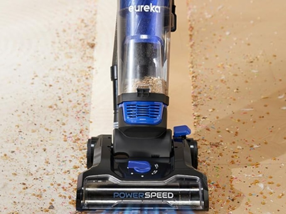 black and blue Eureka vacuum up close pic as it cleans a dirty floor