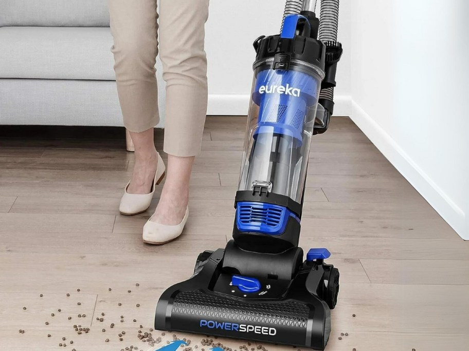 woman vacuuming a hardwood floor with a blue and black Eureka vacuum