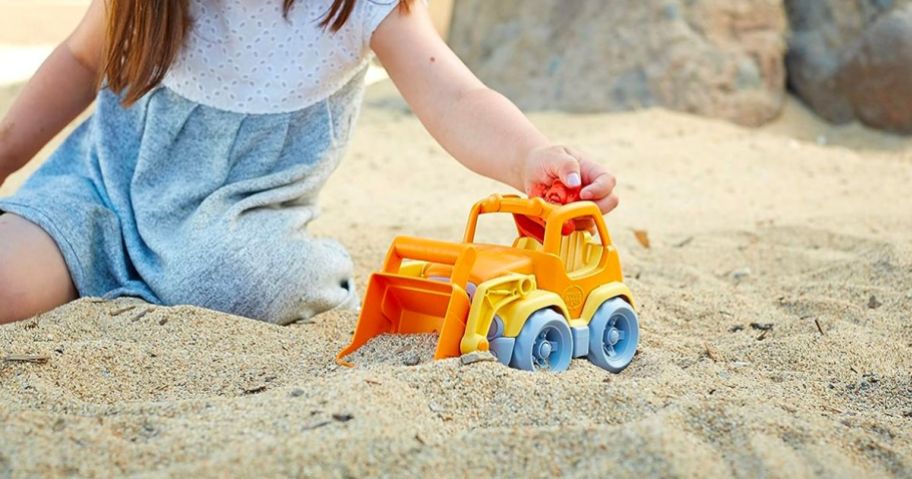 girl playing with orange truck in sand