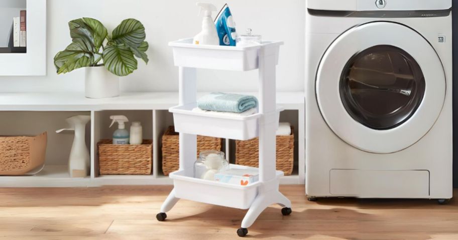 3 tier white plastic utility cart with laundry items in it in a laundry room
