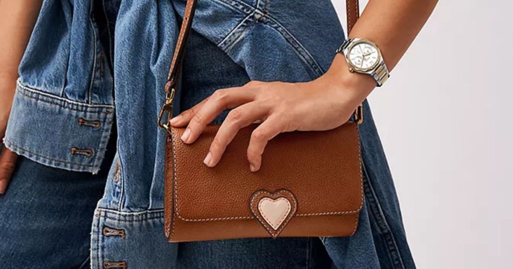 woman wearing a Fossil watch and carrying a Fossil brown crossbody with a pink heart