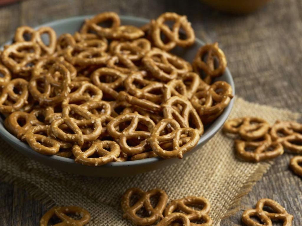 A bowlful of mini pretzels and a few spilling onto the table 