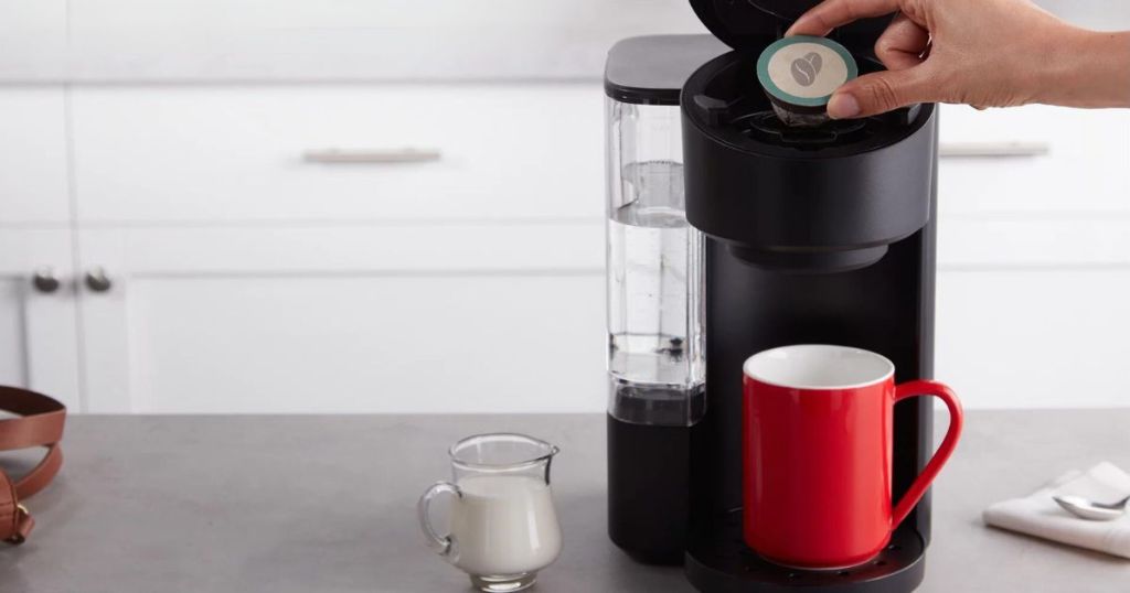 person putting pod in instant solo cafe coffee maker on counter in kitchen
