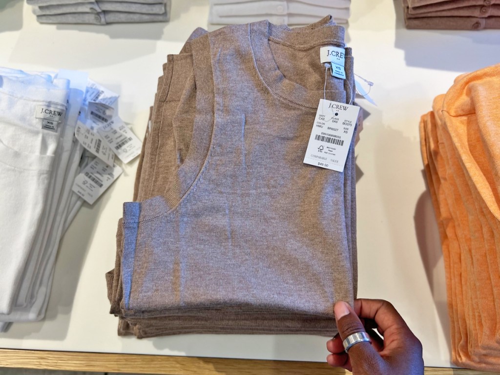 hand touching a folded brown top on store display