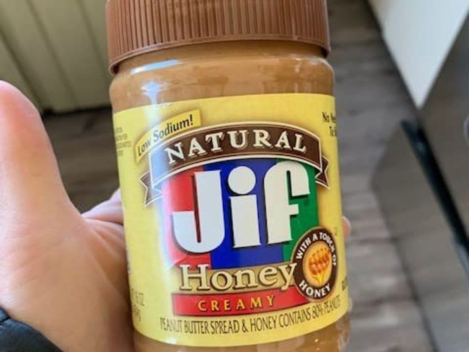 Hand holding a jar of Jif Natural Honey peanut Butter