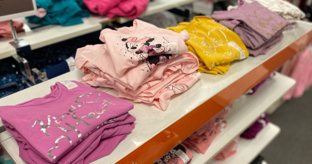 A Kohl's store shelf with stacks of folded Jumping Beans girls shirts on them