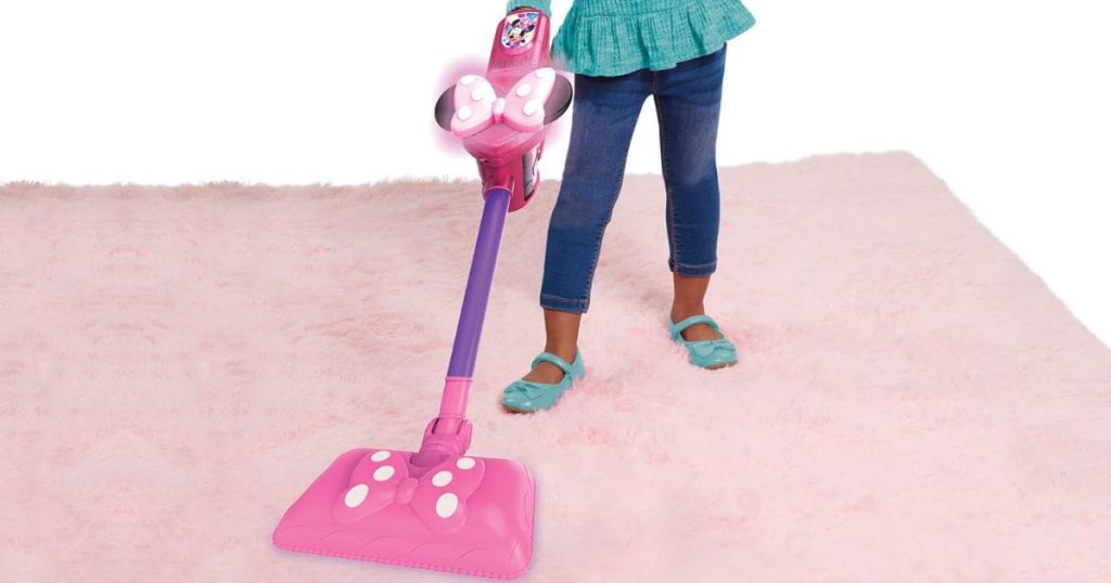Little girl playing with a Just Play Minnie Vacuum on a carpet