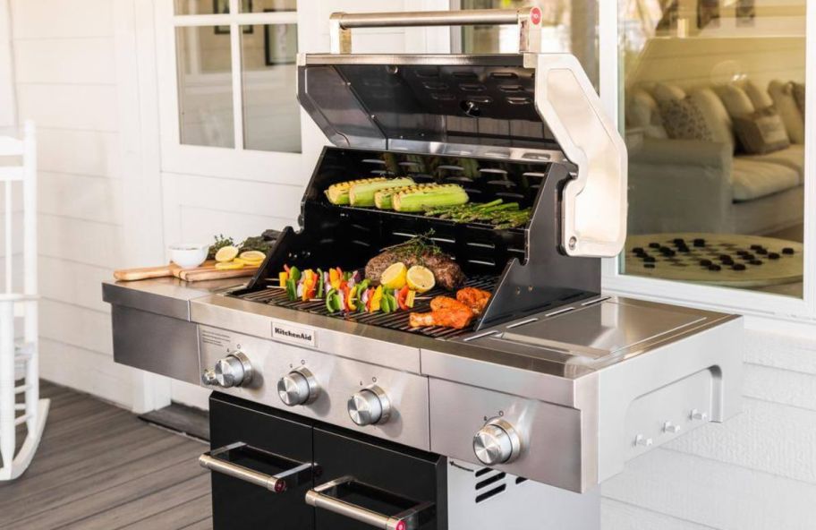 a larger 3 burner propane grill shown with lid raised and assorted foods cooking