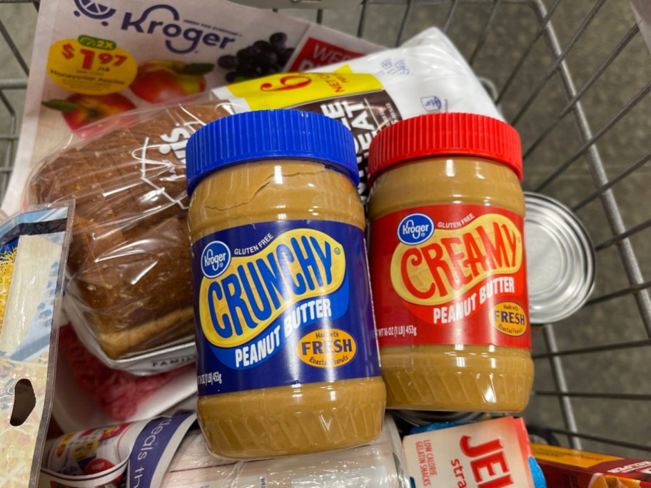 two jars of kroger peanut butter on top of groceries in shopping cart
