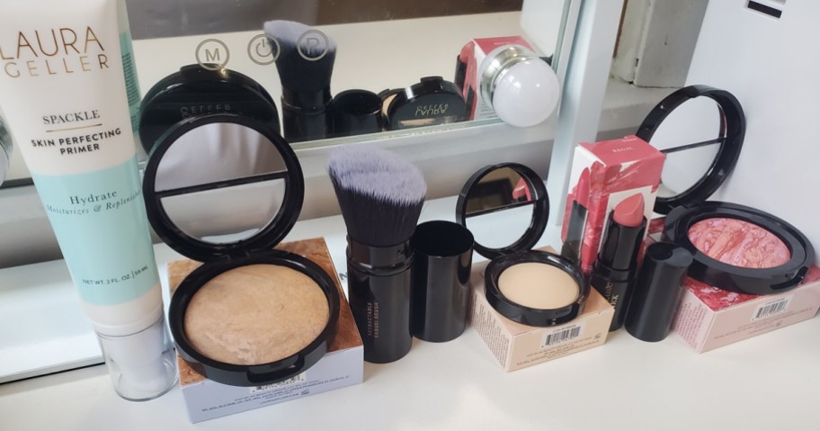 various laura geller makeup products on white table in front of a mirror