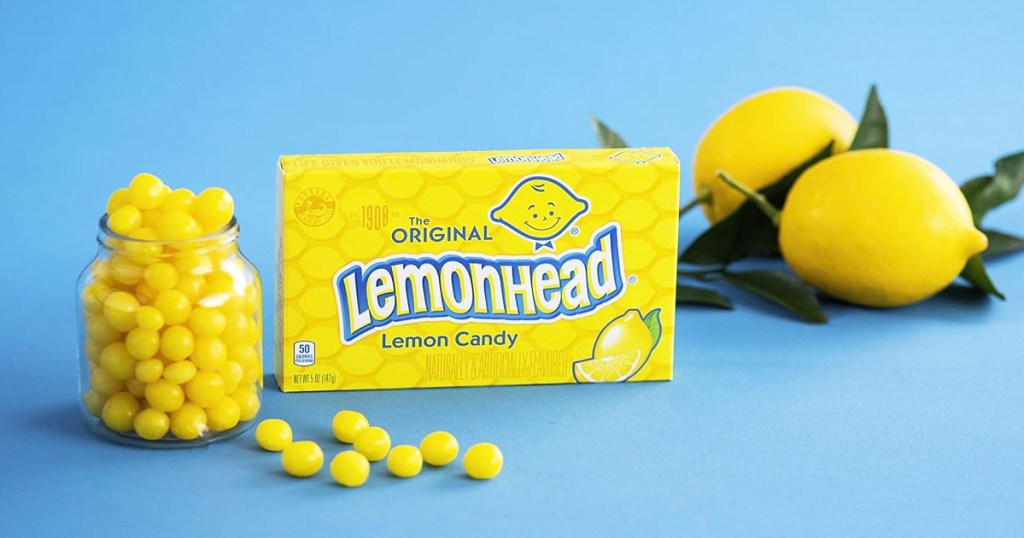 box of lemonhead candy with jar of candies in front of it and lemons in background