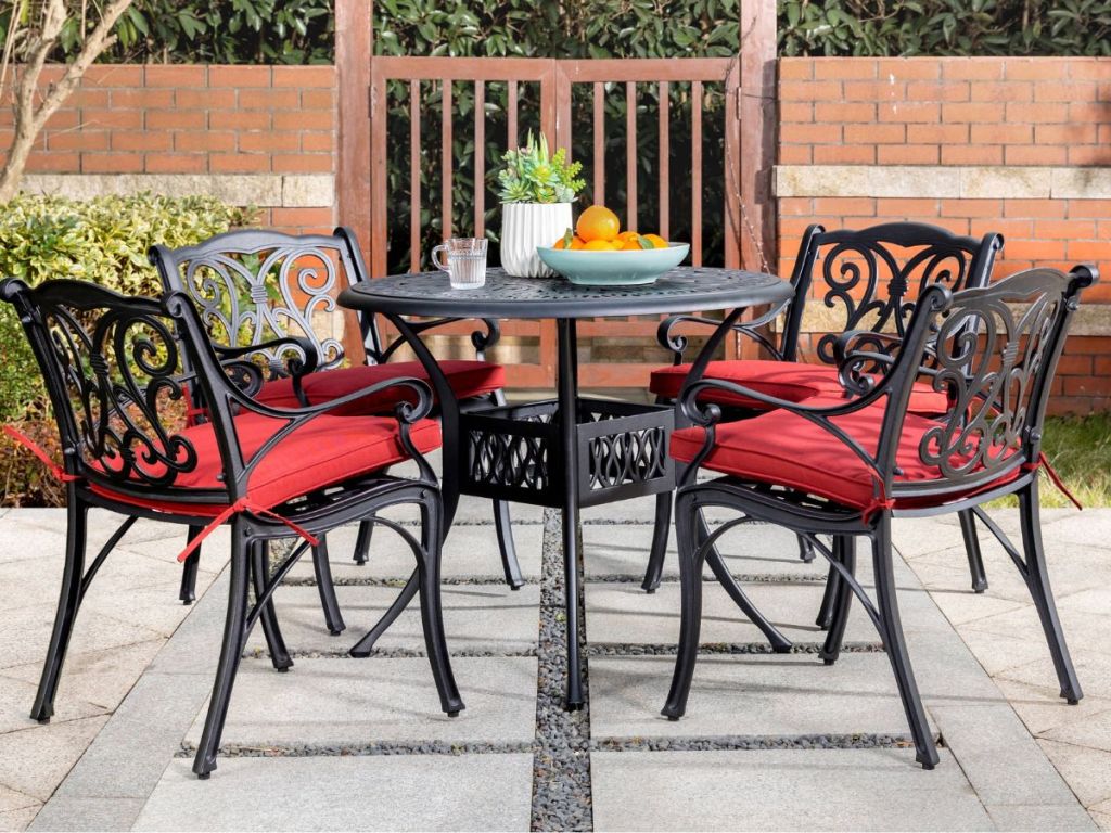 A patio dining set on a porch with a table and four chairs with red cushions