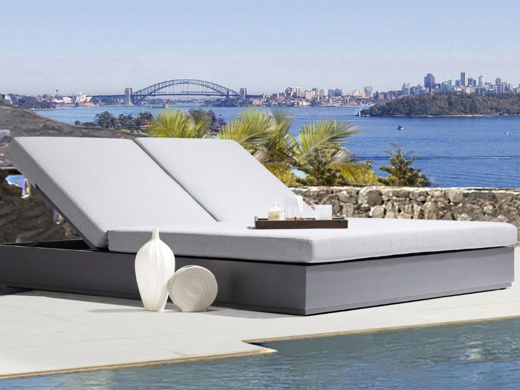 An outdoor double chaise lounge for the patio with a bay in the background