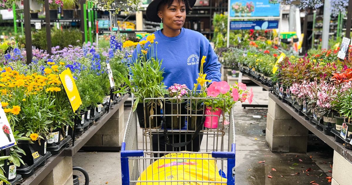 a woman pushing a cart thru the Lowes garden dept with flowers and potting soil in the cart