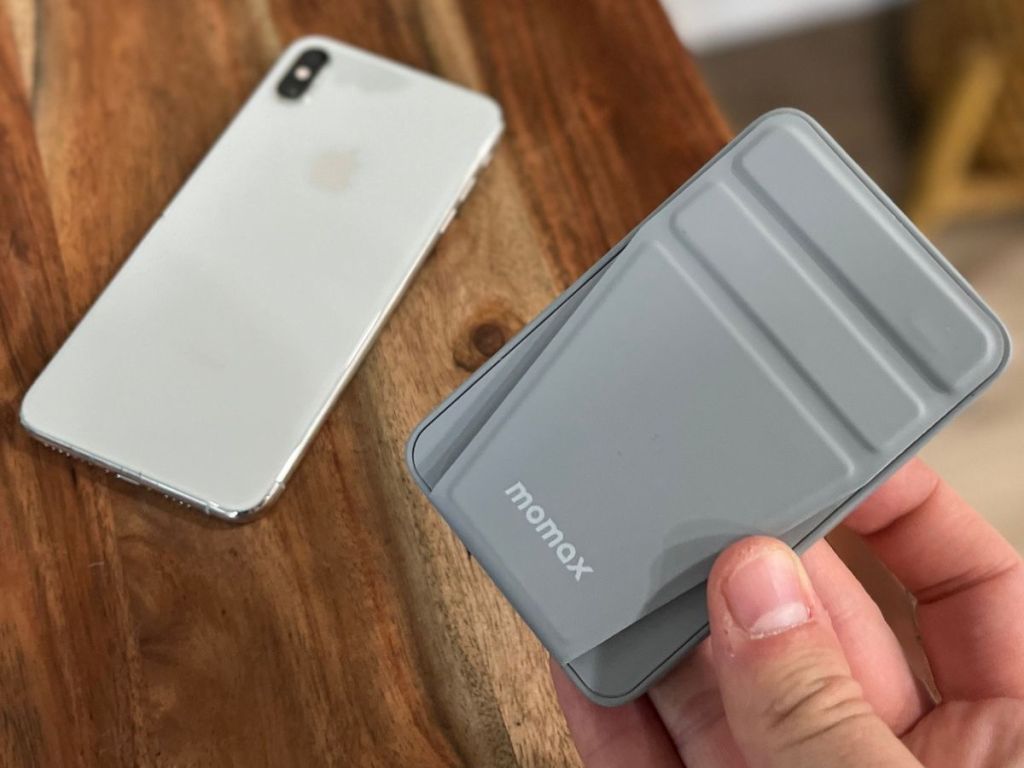 Hand holding a Momax portable charger with an iPhone in the background
