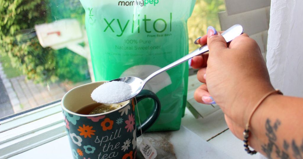 hand placing a tablespoon of morning pep xylitol into a cup of coffee