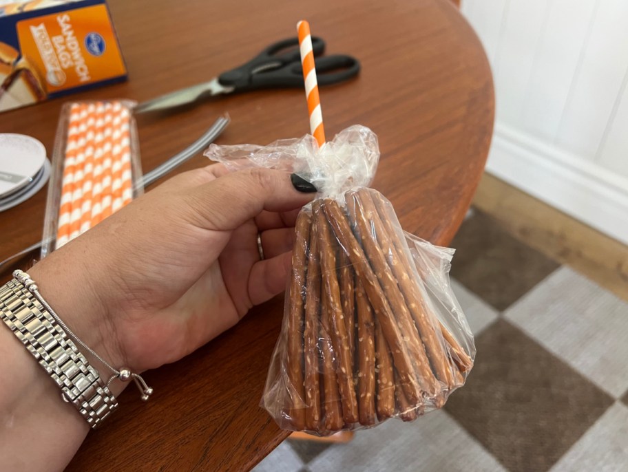 Hand holding a bag of pretzels shaped like a witch broomstick