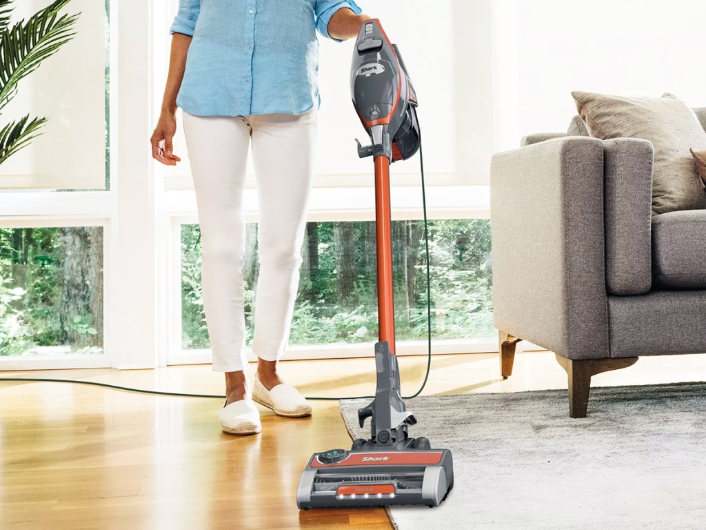 woman using orange and grey stick vacuum on floor