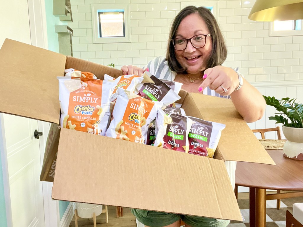 woman holding up a box of Simply Doritos & Cheetos 