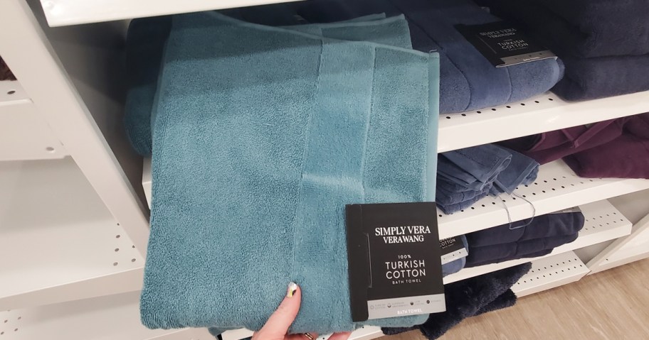 hand grabbing a blue bath towel from store shelf