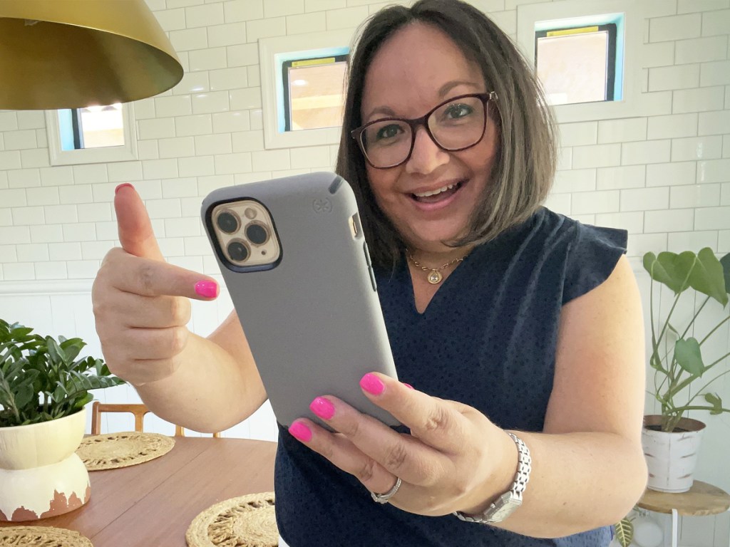 woman holding up and pointing to iphone in a grey case