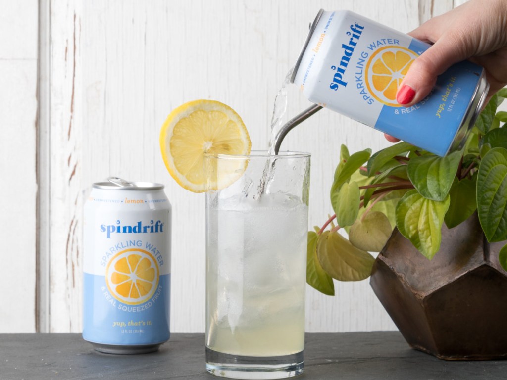 pouring can of spindrift sparkling water into glass with a slice of lemon on rim