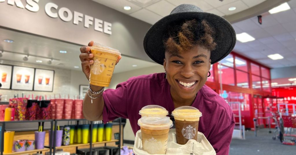 A woman holding Starbucks drinks in a carrier smiling 