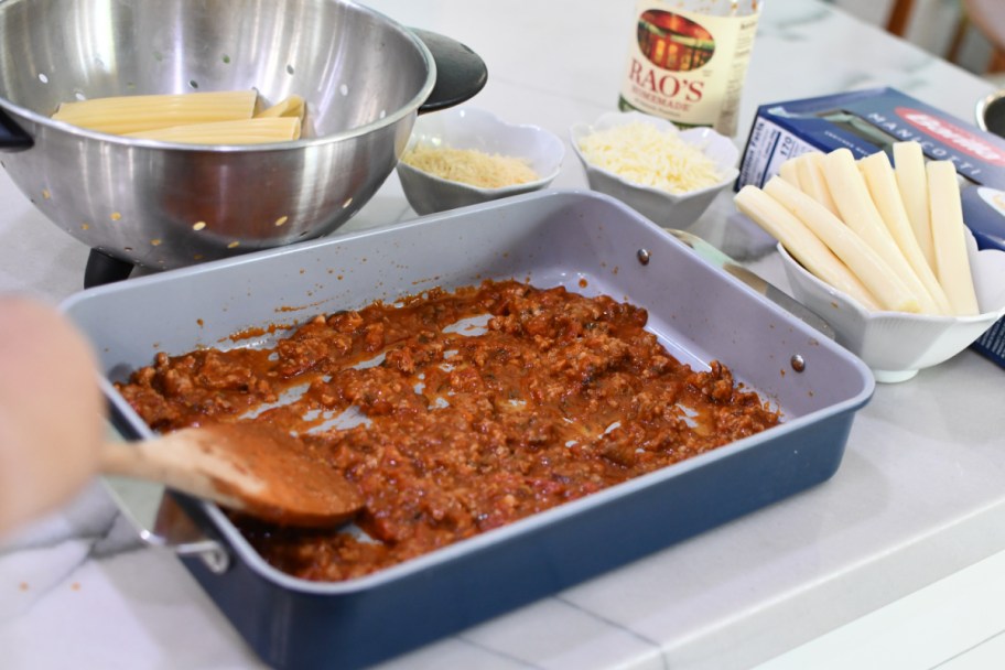 Adding tomato sauce and sausage to a casserole dish in order to make string cheese manicotti