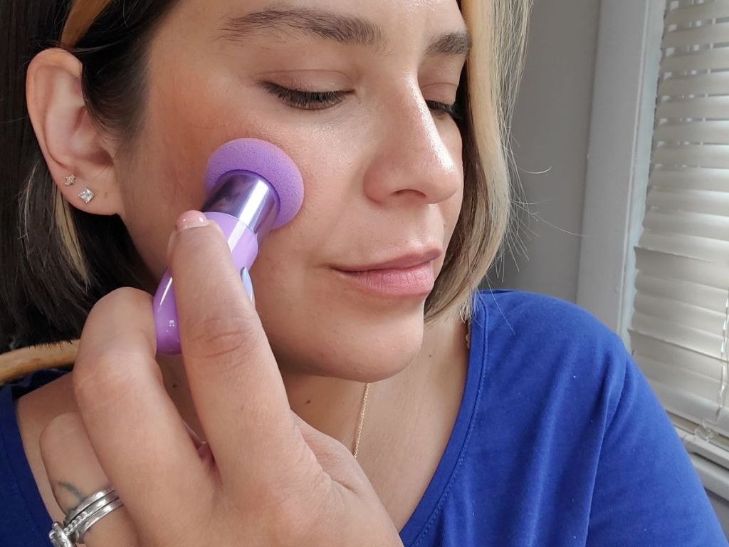 woman using a beauty sponge with a handle to apply blush