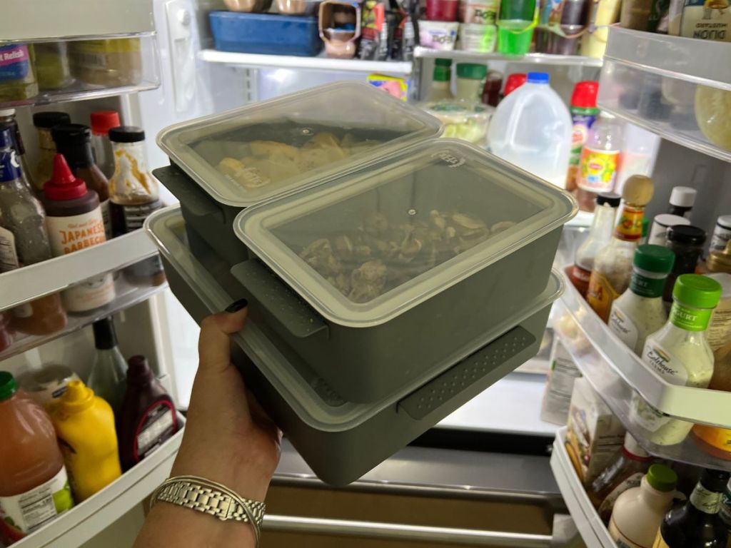 person putting 3 containers with lids carrying food into fridge