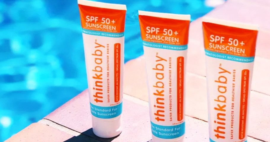three tubes of thinkbaby sunscreen on deck near water