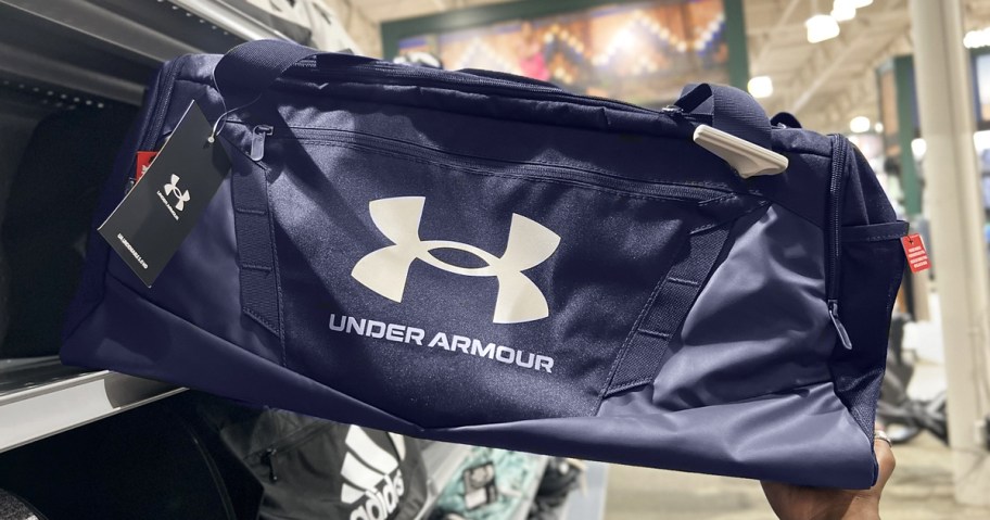 hand grabbing a blue under armour duffle bag from store shelf