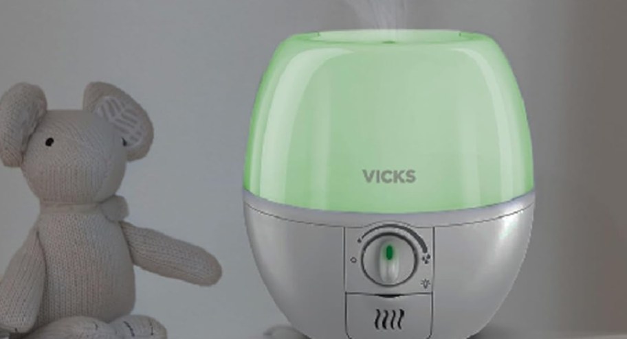 Vicks cool air diffuser with green nightlight on and teddy bear next to it