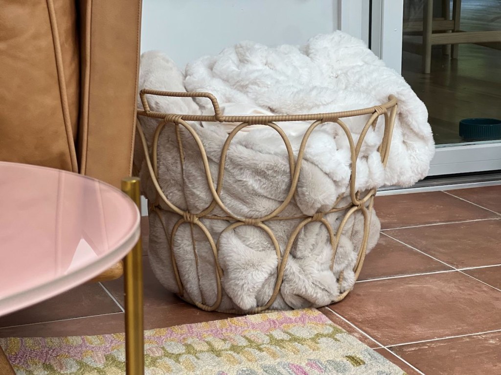 rattan woven basket with white fluffy blanket inside sitting on wood floor