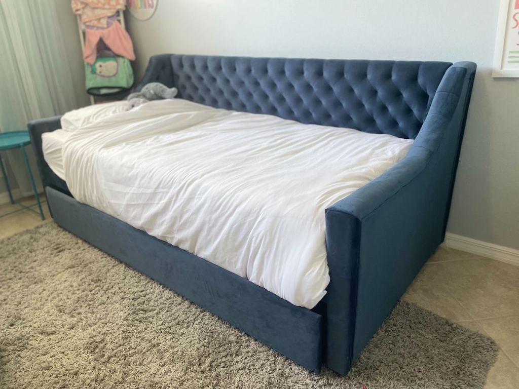 blue tufted daybed with white sheets in room against wall
