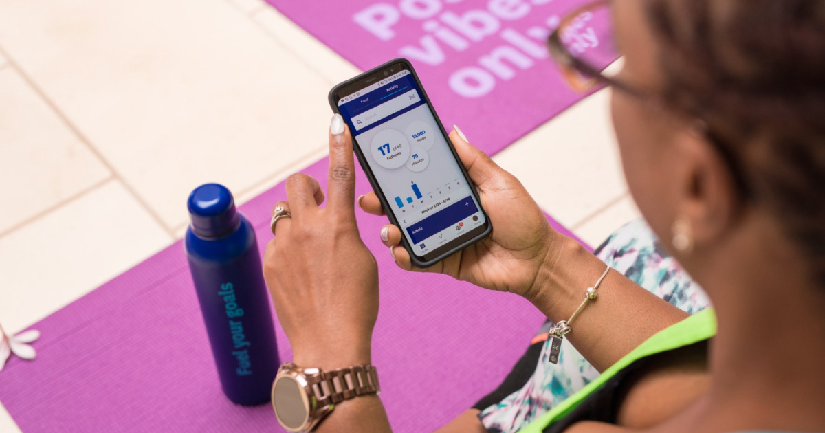 woman using weight watchers app while sitting with water bottle and exercise mats
